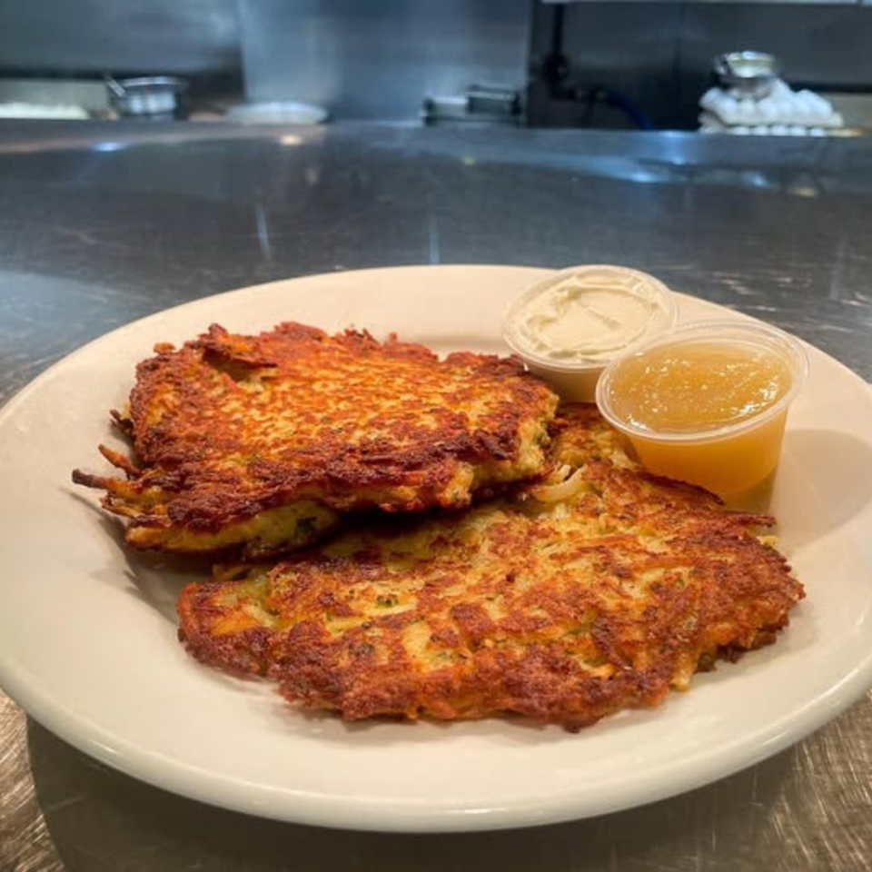 Two golden-brown potato pancakes with sides of applesauce and sour cream on a white plate.